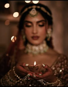 a woman holding a lit candle in her hands while wearing a bridal outfit and jewelry