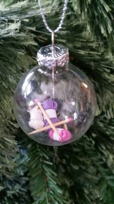 a glass ornament hanging from a christmas tree with yarn and knitting needles in it