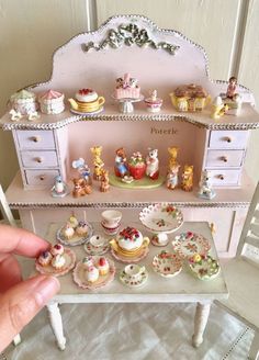 someone is holding their finger up to a dollhouse shelf filled with cupcakes and cakes