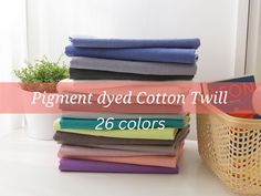 a pile of folded clothes next to a basket with a plant in it and the words, pigment dyed cotton twill 26 colors