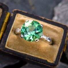 a ring with a green stone in it sitting on top of a velvet box next to some rocks