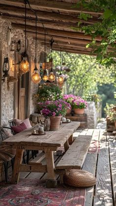 a wooden table sitting on top of a porch next to flowers and potted plants