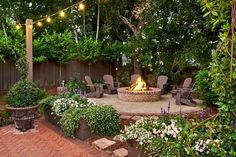 an outdoor fire pit surrounded by greenery and chairs with string lights strung over it