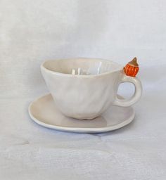 a white cup and saucer with an orange decoration on the side sitting on a white tablecloth