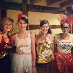 four women dressed in costumes posing for a photo with one holding a bag of candy