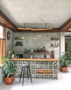 an outdoor bar with potted plants on the counter and hanging lights above it, along with two stools