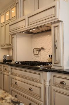 a kitchen with white cabinets and black counter tops, an oven in the middle is shown