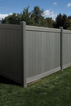 a large gray fence in the middle of a grassy area with trees and bushes behind it