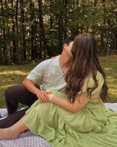 a man and woman sitting on top of a blanket in the grass kissing each other