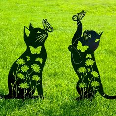 two black cats sitting in the grass with butterflies on their heads and one has its paws up