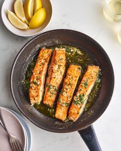 three salmon fillets in a skillet with lemons and water on the side