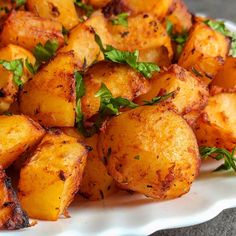 a white plate topped with cooked potatoes and garnished with parsley on top