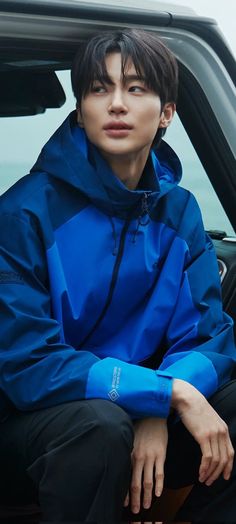 a young man sitting in the passenger seat of a car wearing a blue jacket and black pants