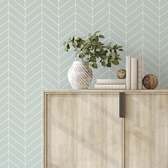 a white vase sitting on top of a wooden cabinet next to a wallpapered wall