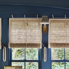 two windows with roman shades hanging from them in front of a blue wall and window sill