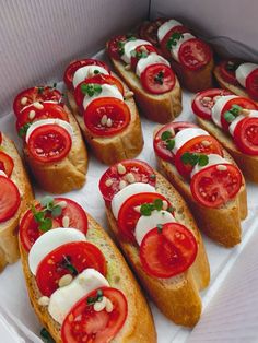 several slices of bread with tomatoes and cheese on them in a white cardboard box lined up