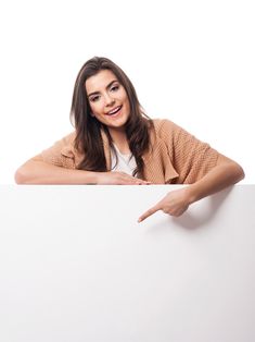 a woman leaning on a white board pointing to the side with her finger and smiling