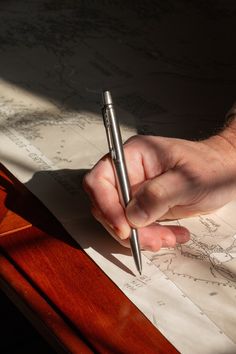 a person holding a pen and writing on a piece of paper with the sun shining through