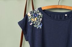 a t - shirt hanging on a wooden hanger next to a green wall with flowers