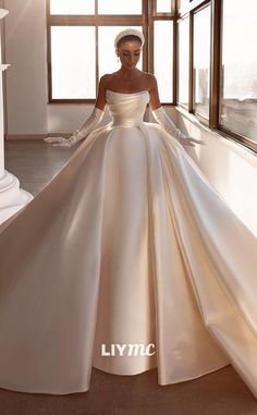 a woman in a white gown standing by a window with her hands on her hips