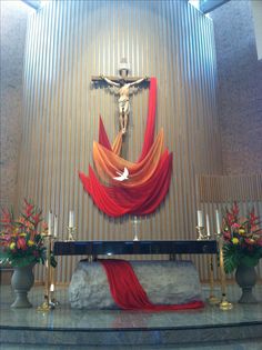 the altar is decorated with red drapes and flowers in front of a crucifix