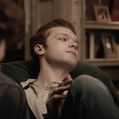 a young man sitting on top of a couch in front of a book shelf and looking up