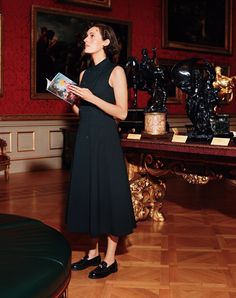 a woman in a black dress is reading a book and looking up at the ceiling