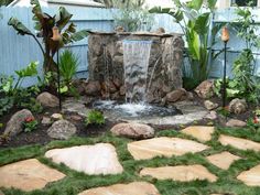 a small waterfall in the middle of a garden with rocks and grass on the ground