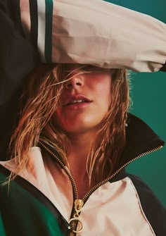 a woman with long hair wearing a white and green jacket, black hoodie and gold zipper around her neck