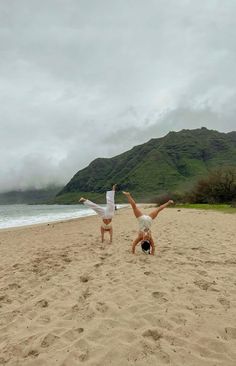 two people doing handstands on the beach with mountains in the background