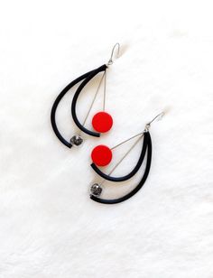 two red and black earrings are hanging on a white furnishing surface with silver beads