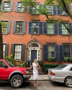 a woman standing in front of a red brick building with blue shutters on the windows