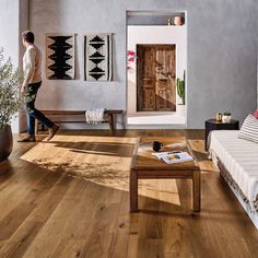 a man walking through a living room filled with furniture and decor on top of hard wood flooring