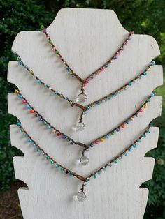 three necklaces with different colored beads on a wooden stand in front of some bushes