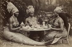 three women dressed as mermaids sitting at a table with tea cups and saucers