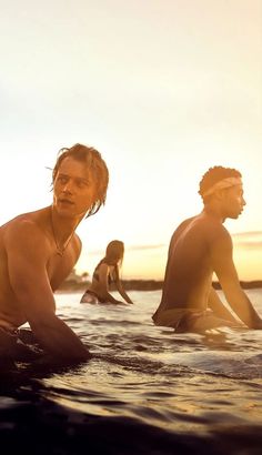 three surfers in the water at sunset