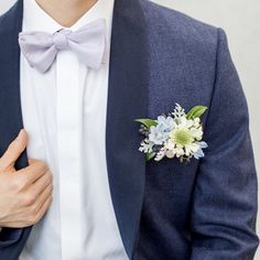 a man in a blue suit and bow tie with a boutonniere on his lapel