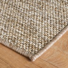 a close up view of the top of a rug on a wooden floor with white and beige colors