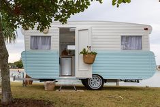 a small blue and white trailer parked next to a tree in front of a body of water