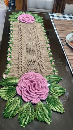 the table is covered with crochet and has pink flowers on it, along with green leaves