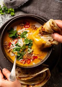 someone is dipping tortilla into a bowl of soup with cheese and other toppings