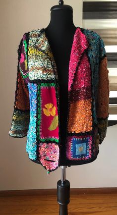 a mannequin wearing a colorful jacket on top of a wooden table next to a window