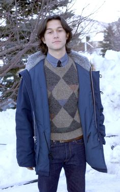 a man standing in the snow wearing a blue jacket and tie with his hands in his pockets