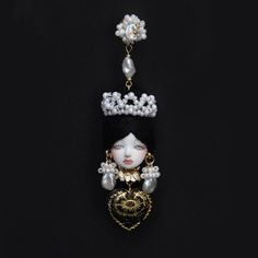 a necklace with pearls and a doll on it's head, hanging from a black background