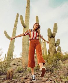 a woman standing in front of a cactus with her arms out and legs spread wide