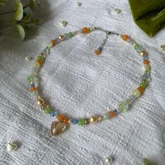 Colourful summer inspired necklace with gold glitter transparent pendant heart, peach, blue, green, yellow and cream crystal and acrylic beads and pearls. Beads used are high quality, strung onto stainless steel flexible wire, finished with a lobster clasp and heart chain.  ♡ care info ♡ To keep your necklace in wonderful condition be gentle when handling, remove before sleeping or showering, and keep away from moisture (perfume, lotion, sweat, ect). ♡ shipping ♡ Please double check your address Necklace Homemade, Necklace Fairycore, Cottagecore Necklace, Fairycore Necklace, Peach Necklace, Homemade Necklaces, Perfume Lotion, Yellow Necklace, Necklace Ideas