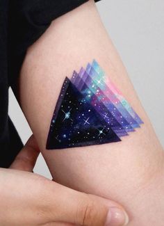 a person's arm with a triangle tattoo on it and stars in the sky