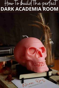 a pink skull sitting on top of a desk next to a book with the title how to build the perfect dark academy room