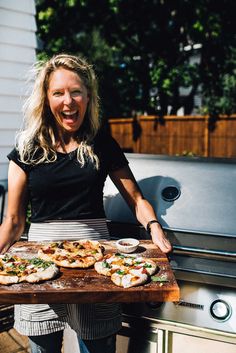 a woman standing in front of an outdoor grill holding a tray of food