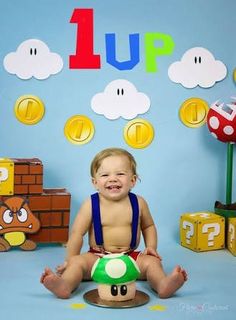 a baby sitting on the ground in front of a backdrop with mario's mushroom